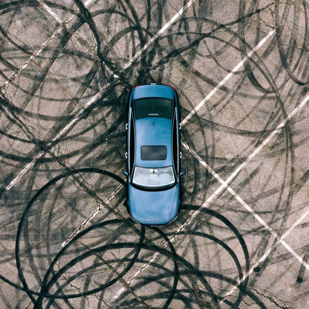 A blue car seen from above on asphalt covered in looping tyre marks.